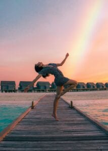 lady dancing on a pier with a rainbow behind her 