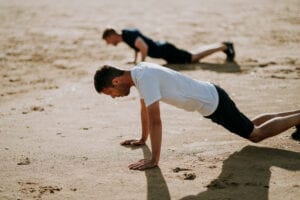 two men doing pushups on the beach 